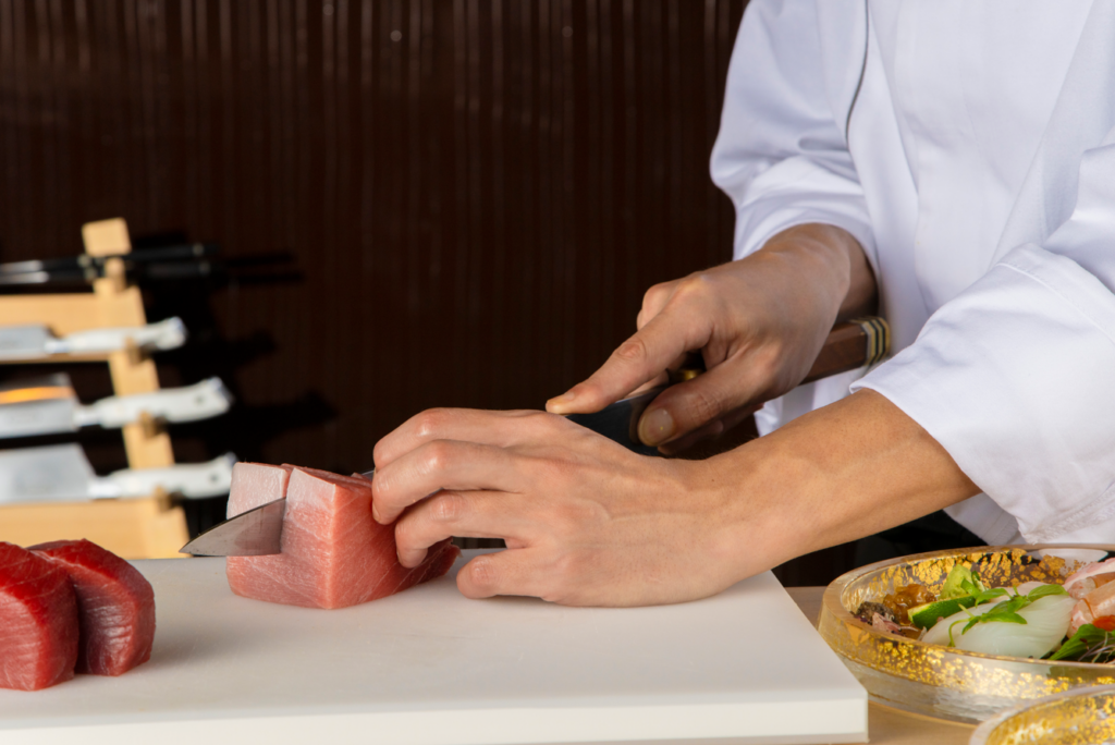 A Japanese chef skillfully slicies a fillet of salmon sashimi.